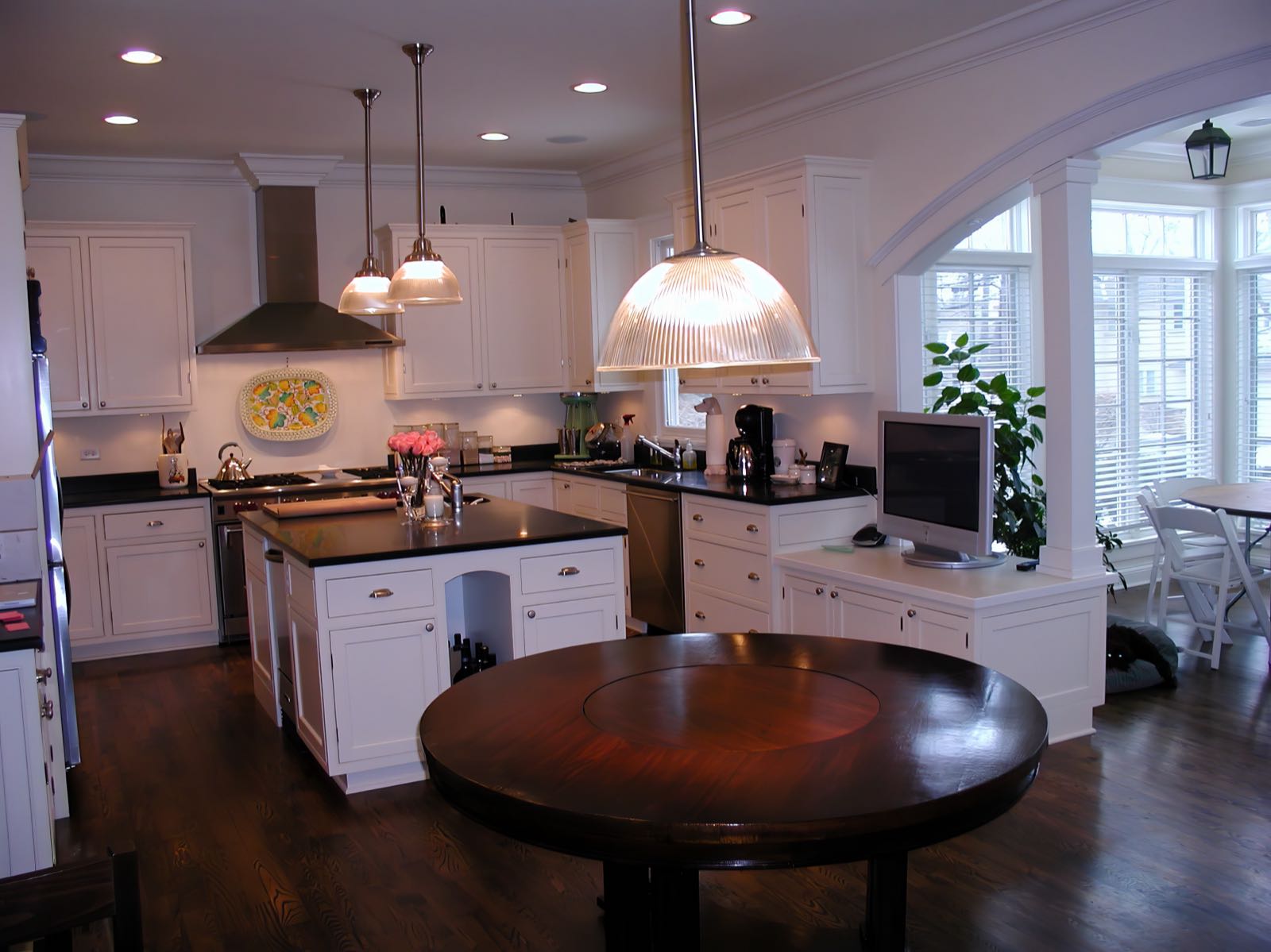 The kitchen from the breakfast area, with a round table in the foreground and an arched bay window beyond.