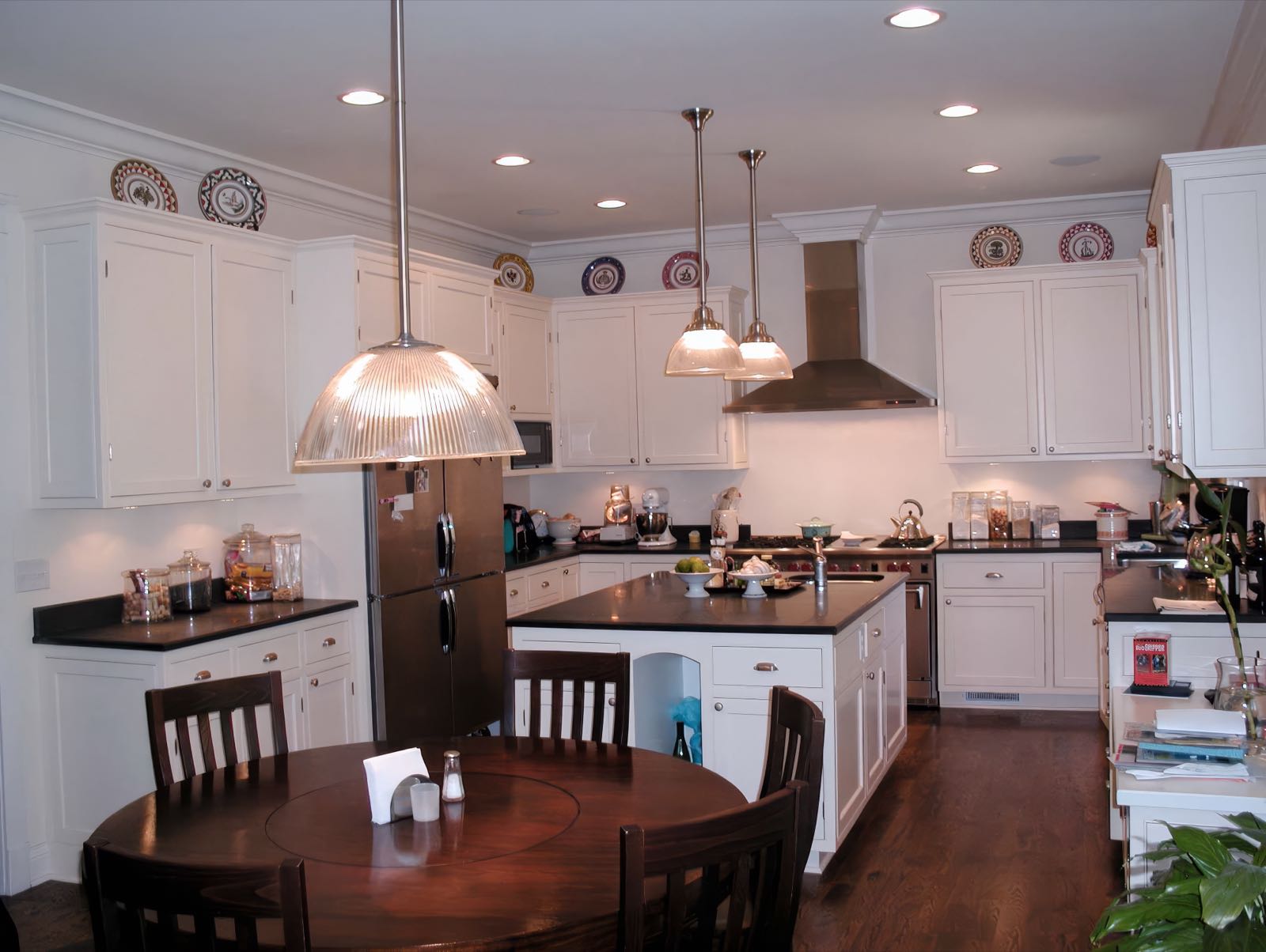Kitchen with white painted cabinetry, dark stone counters, a large island, glass pendants and a run of plate display above the wall units.