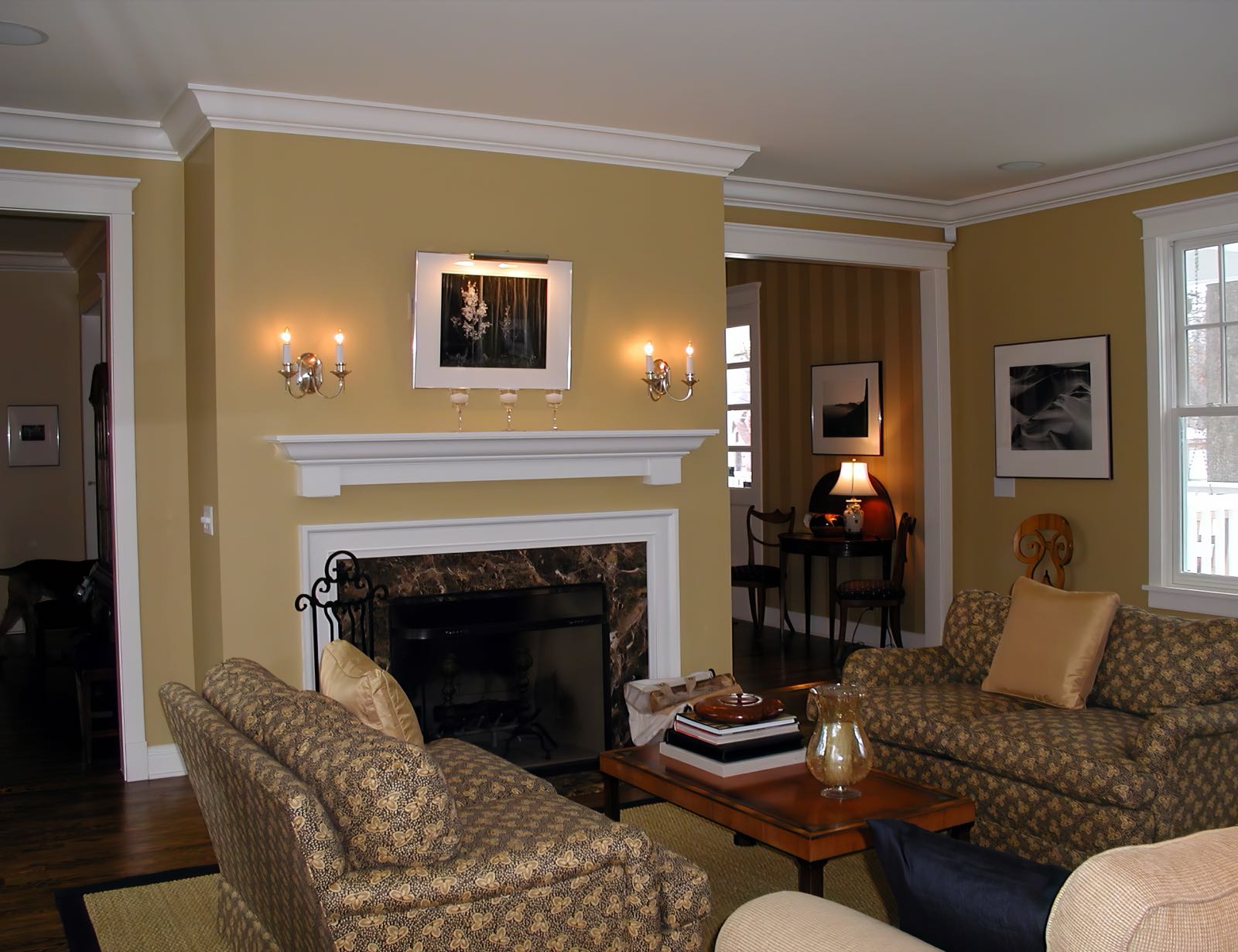 Living room with a stone fireplace under a painted mantel, flanking wall sconces and upholstered seating.