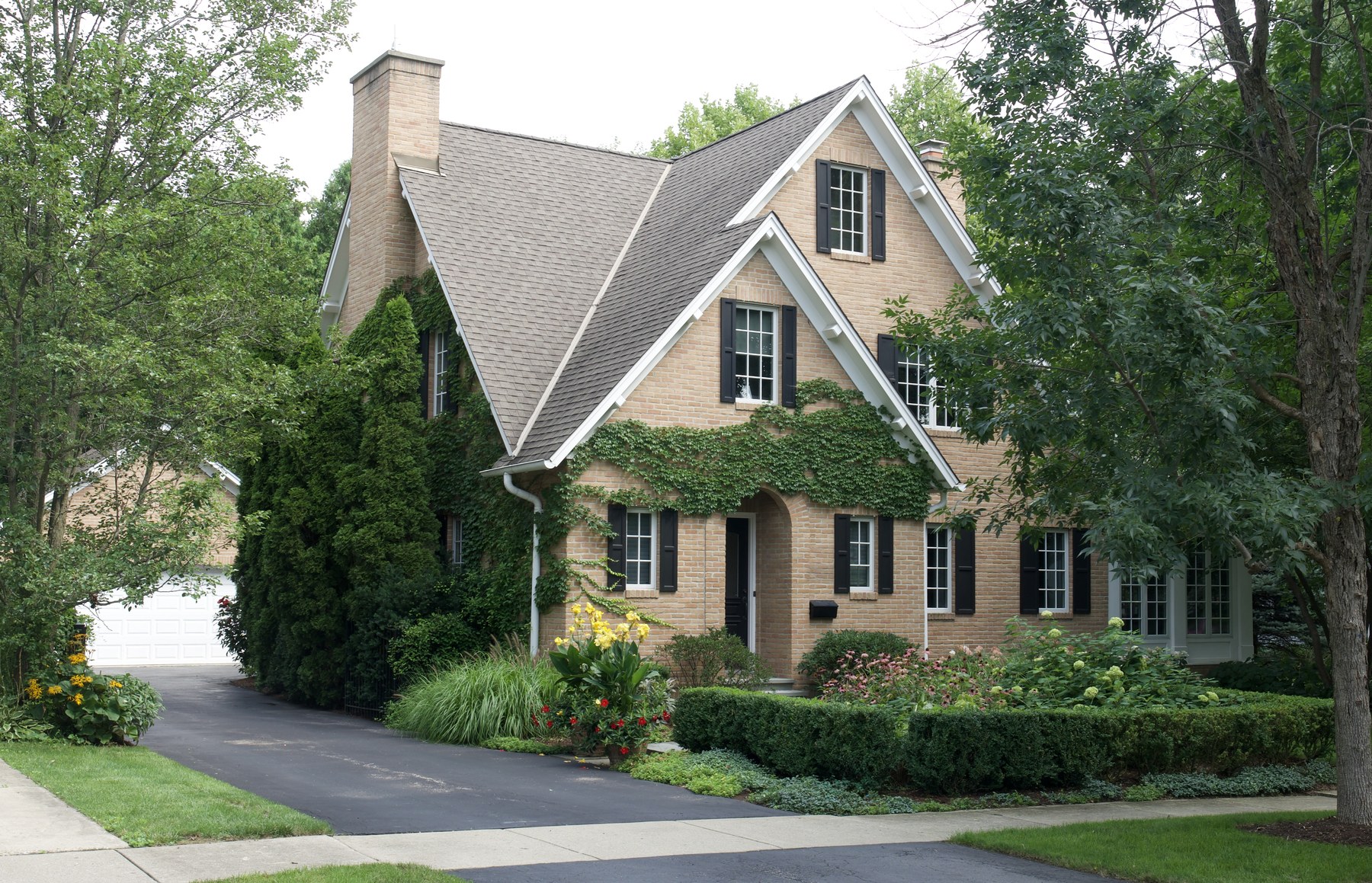 The cottage from the drive, its buff brick gables stepping forward one behind another, with ivy grown across the entry gable and a broad chimney to the left.