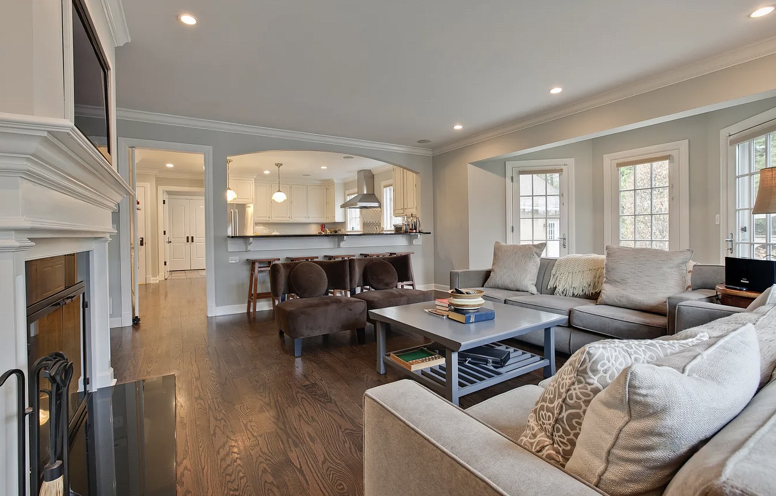 The living room from the opposite end, with a white mantelpiece and black-framed fireplace flanked by built-in cabinets and open shelving.