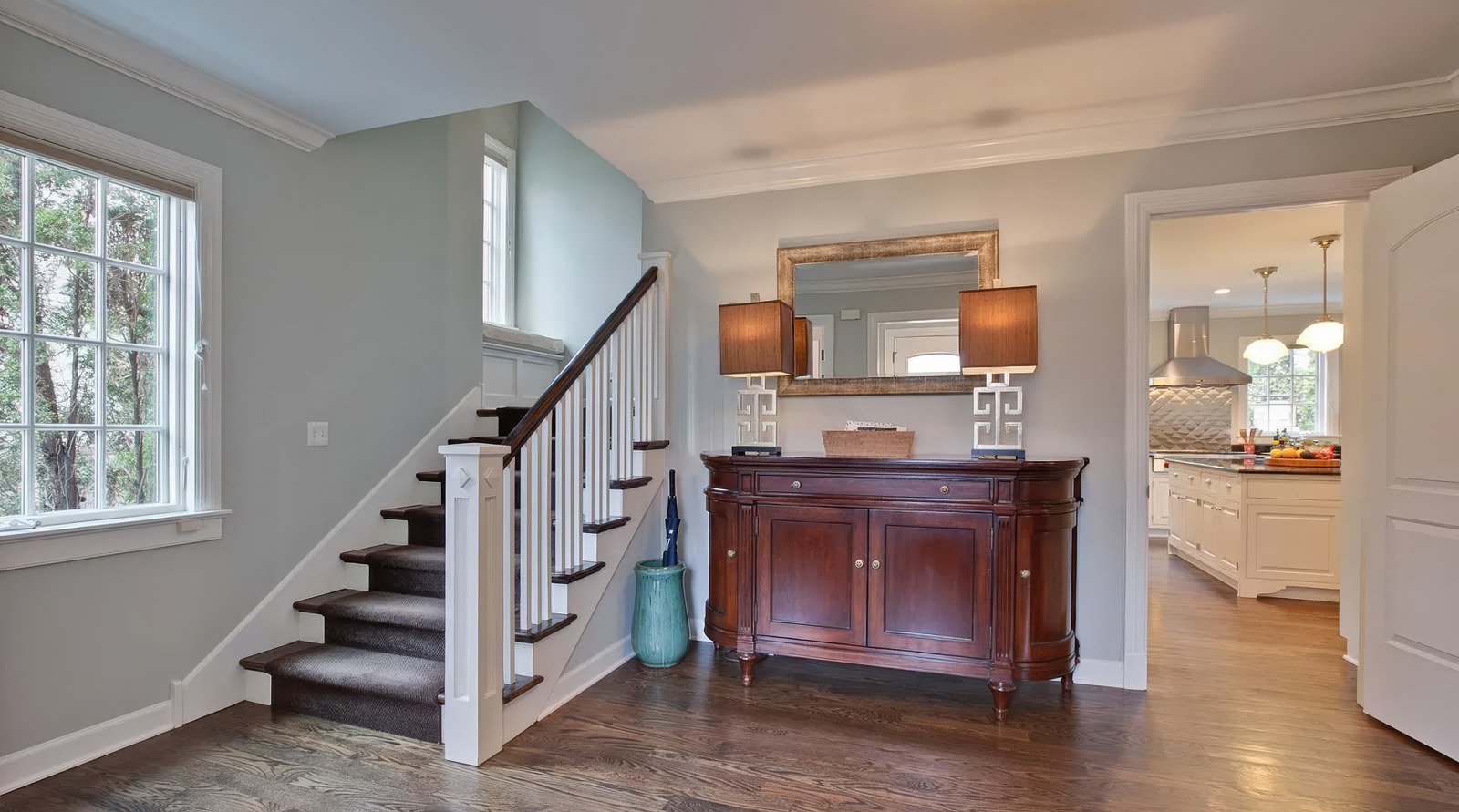 The entrance hall, with a turned stair rising to the left under a tall window and a doorway on the right giving through to the kitchen.