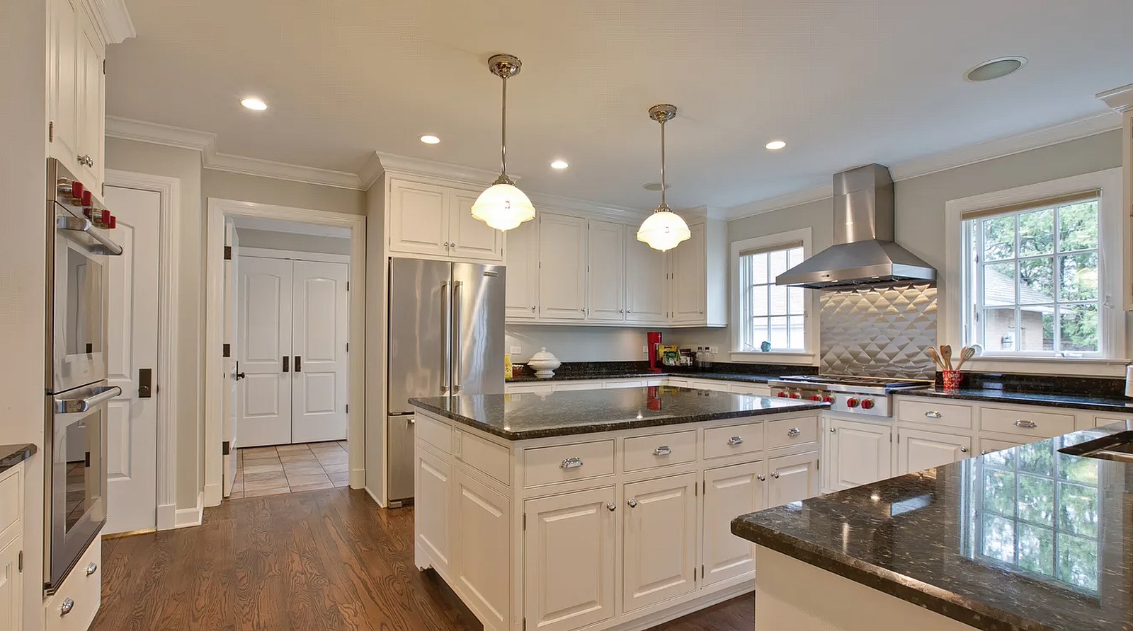 The kitchen looking towards the pantry, with panelled double doors to the rear hall, the refrigerator alongside, and the hood and range at the far wall.