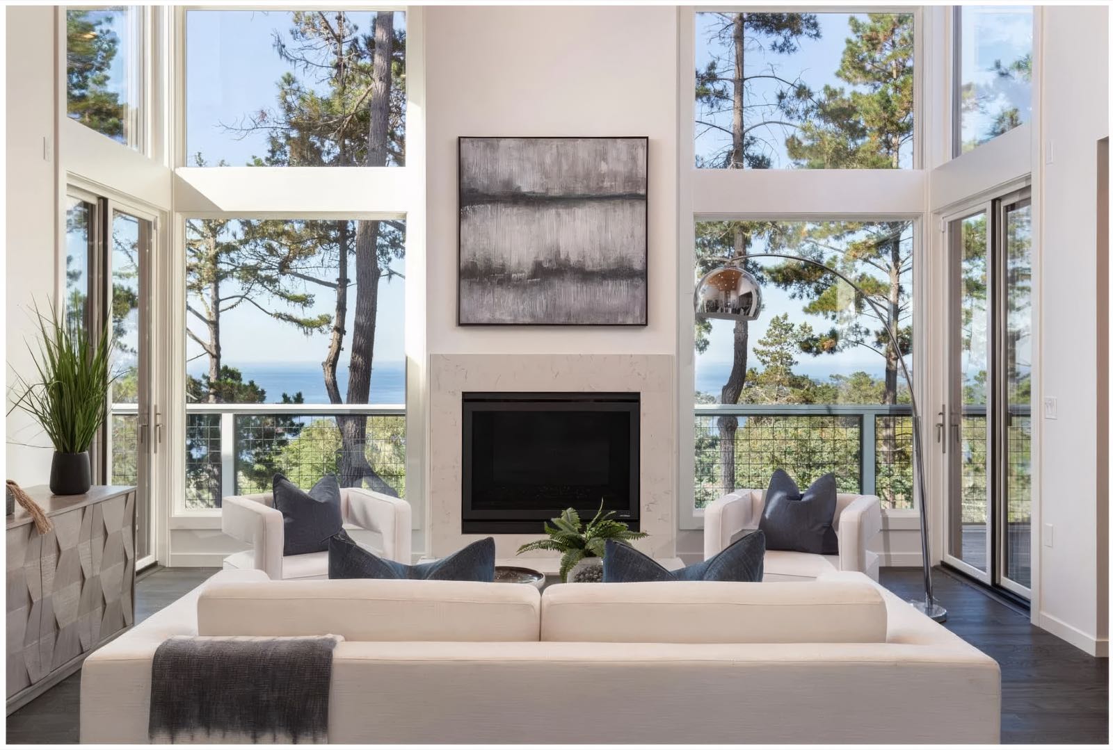 Living room seen straight on, glazing turning both corners to the trees and a strip of ocean.