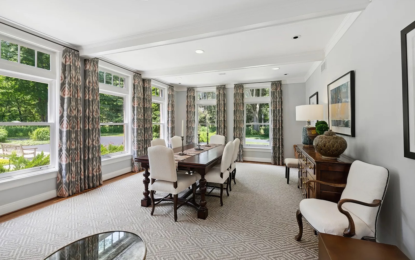 The dining room, with tall windows along two walls looking out to the lawn, and a long table set beneath them.