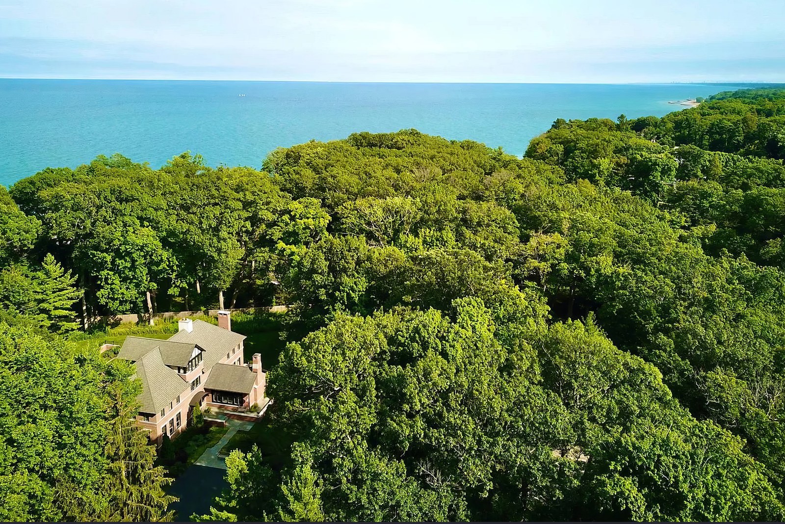 The house from above, almost buried in mature woodland, with the lake beyond the treeline.