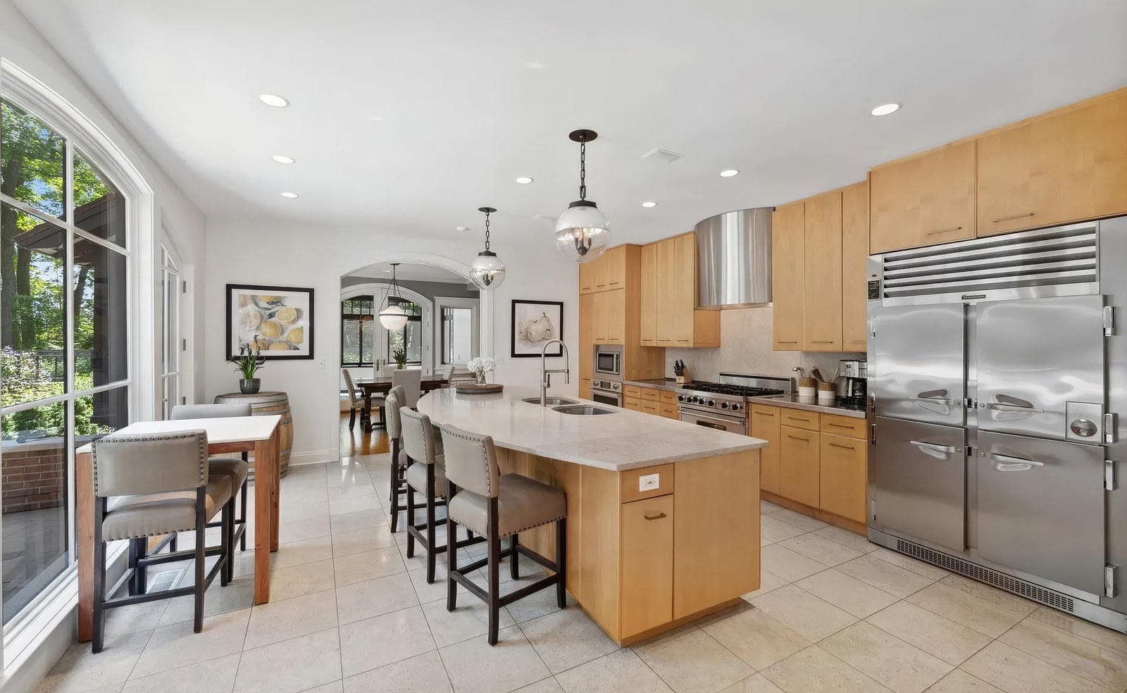 The kitchen, with a long island and seating, maple wall cabinets, a stainless range and hood, and an arched opening through to the breakfast area.
