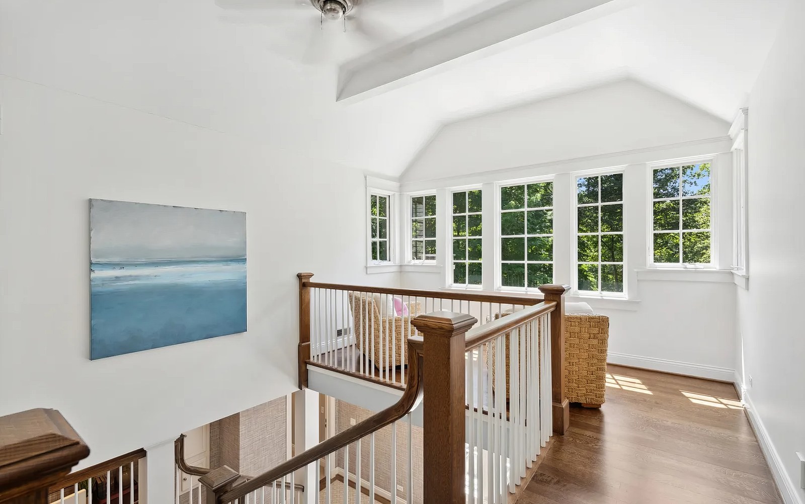 The top-floor landing, lit by a run of windows, with the stair rail returning around an opening down to the floor below.