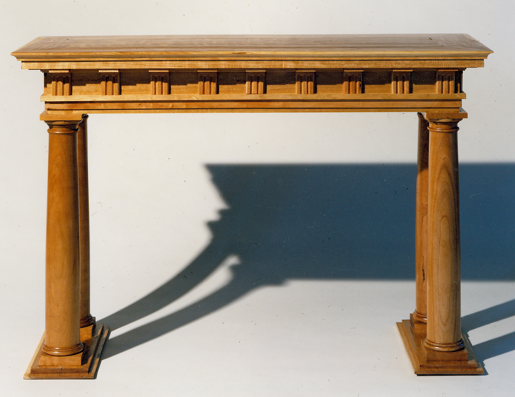 A cherry sofa table carried on two turned Doric columns on stepped plinths, with a frieze of small reeded blocks beneath a moulded top.