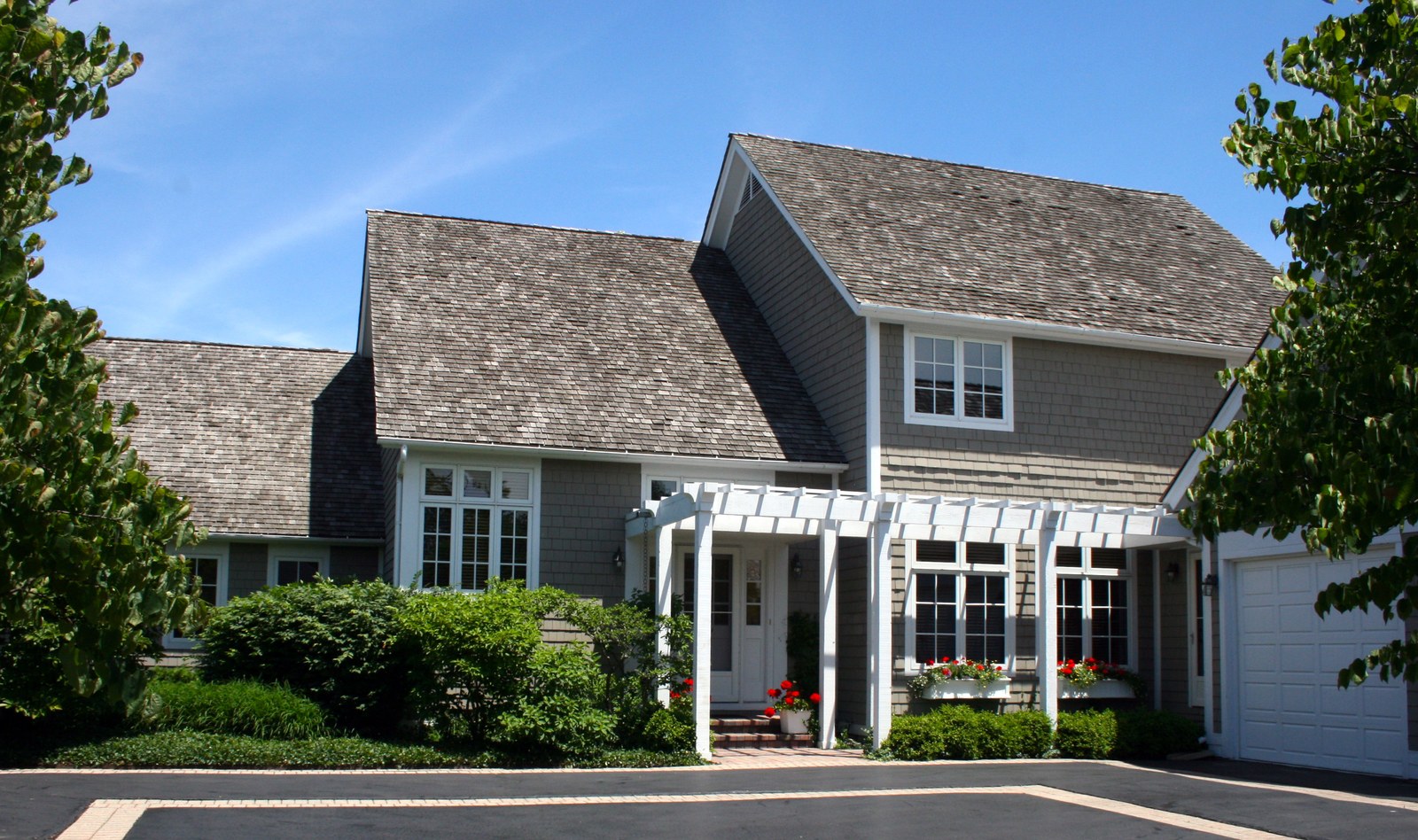 The entry front, a white pergola carried across the door between the shingled wing and the garage, with window boxes in flower.