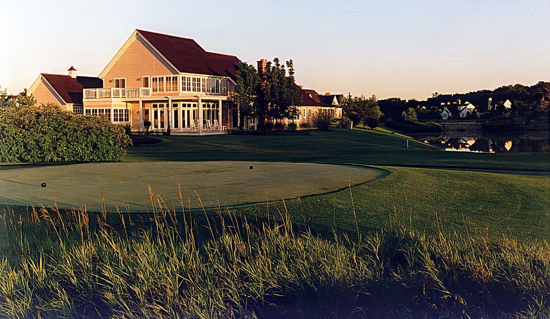 The house seen across the course at sunset, its gable and balcony catching the last light above the green.