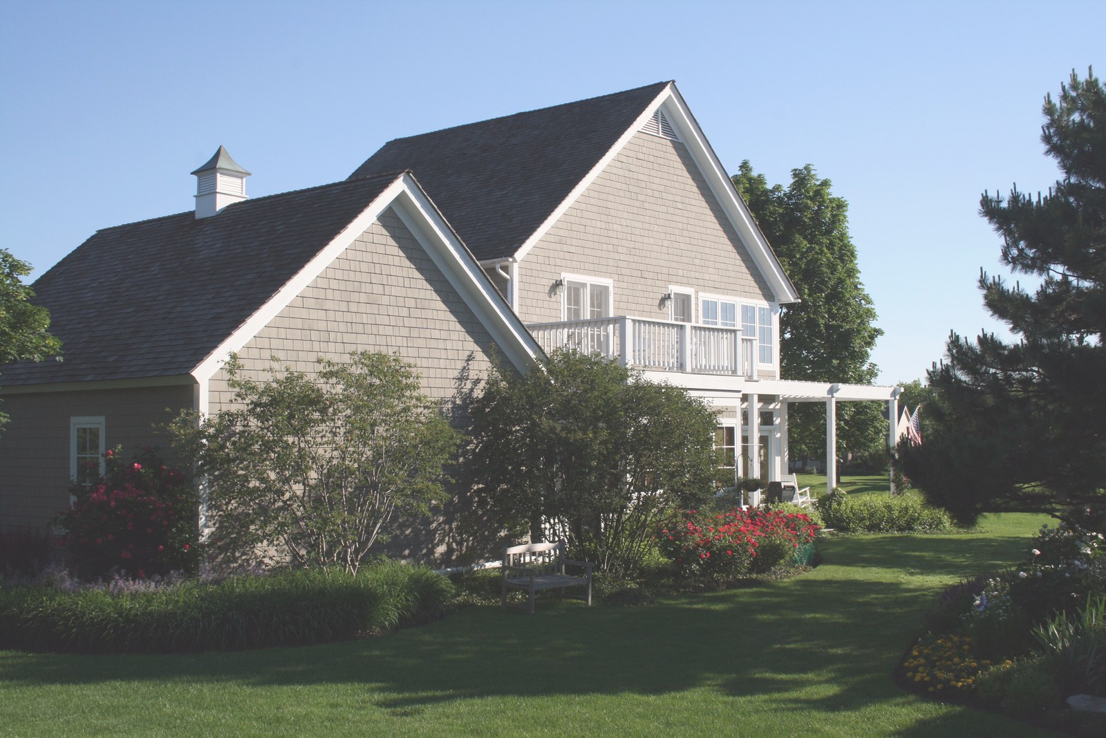 The garden front: two steep shingled gables stepping past one another, a balcony set between them, and a cupola on the low wing behind.