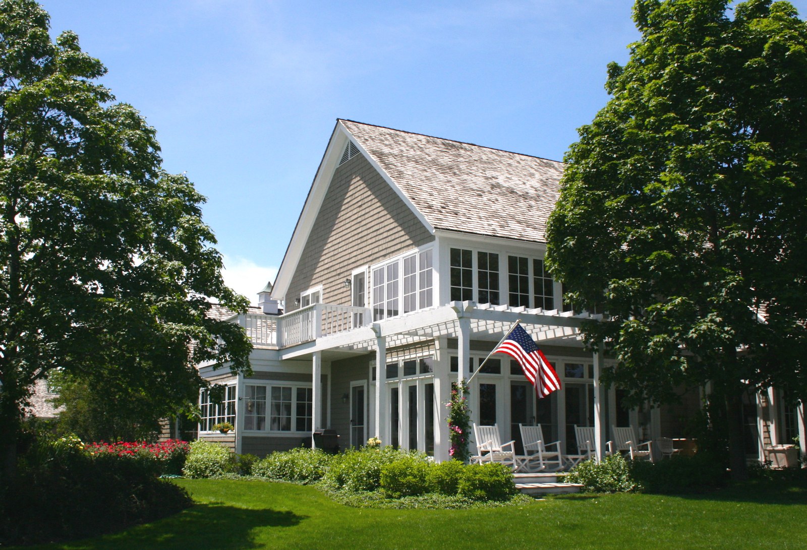 The rear terrace held between the wings of the house, under a white pergola, with rocking chairs along the porch and a flag at the corner.