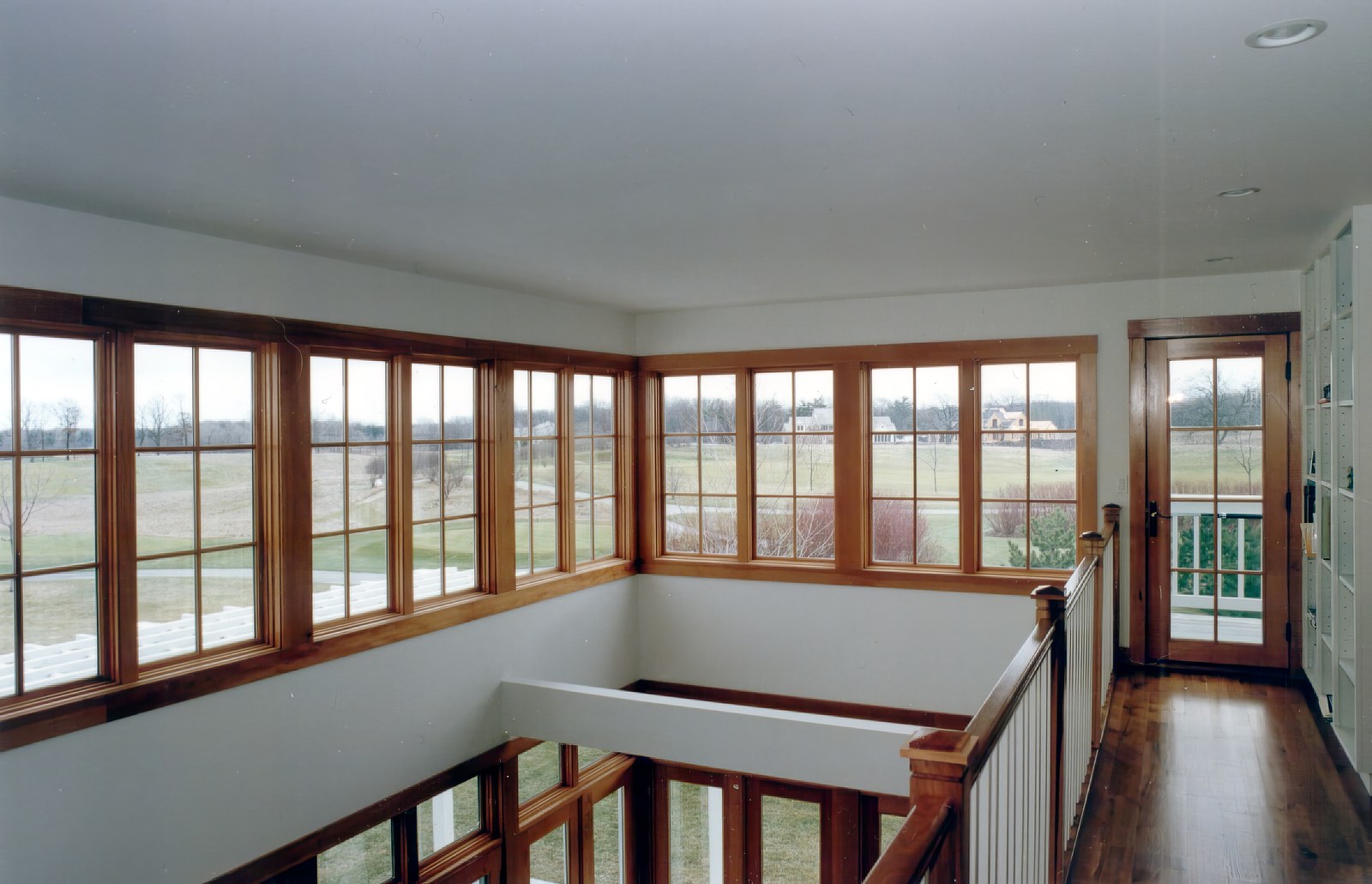 The upper hall, glazed along two sides and open over the living room below, looking out across the fairway.
