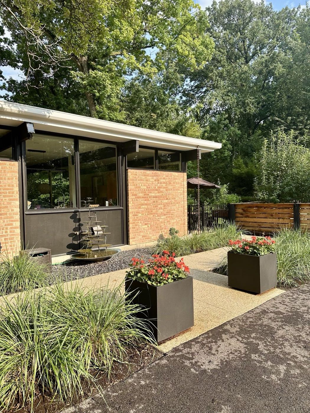 Entry court with a tiered water feature set in gravel, planters of geraniums and clipped grasses against the brick.