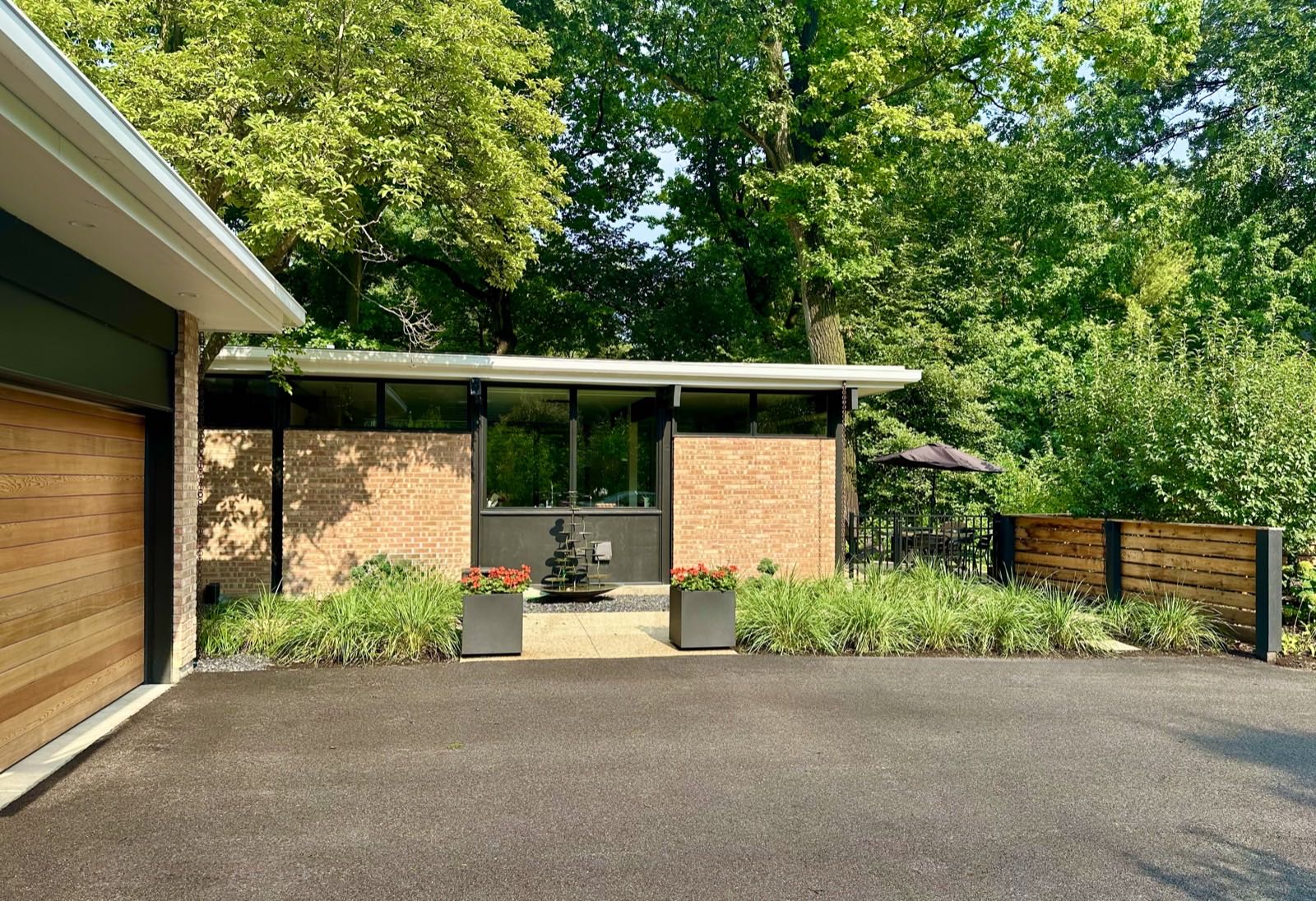 The house from the parking court: cedar garage door at left, brick piers and clerestory glazing across the entry.