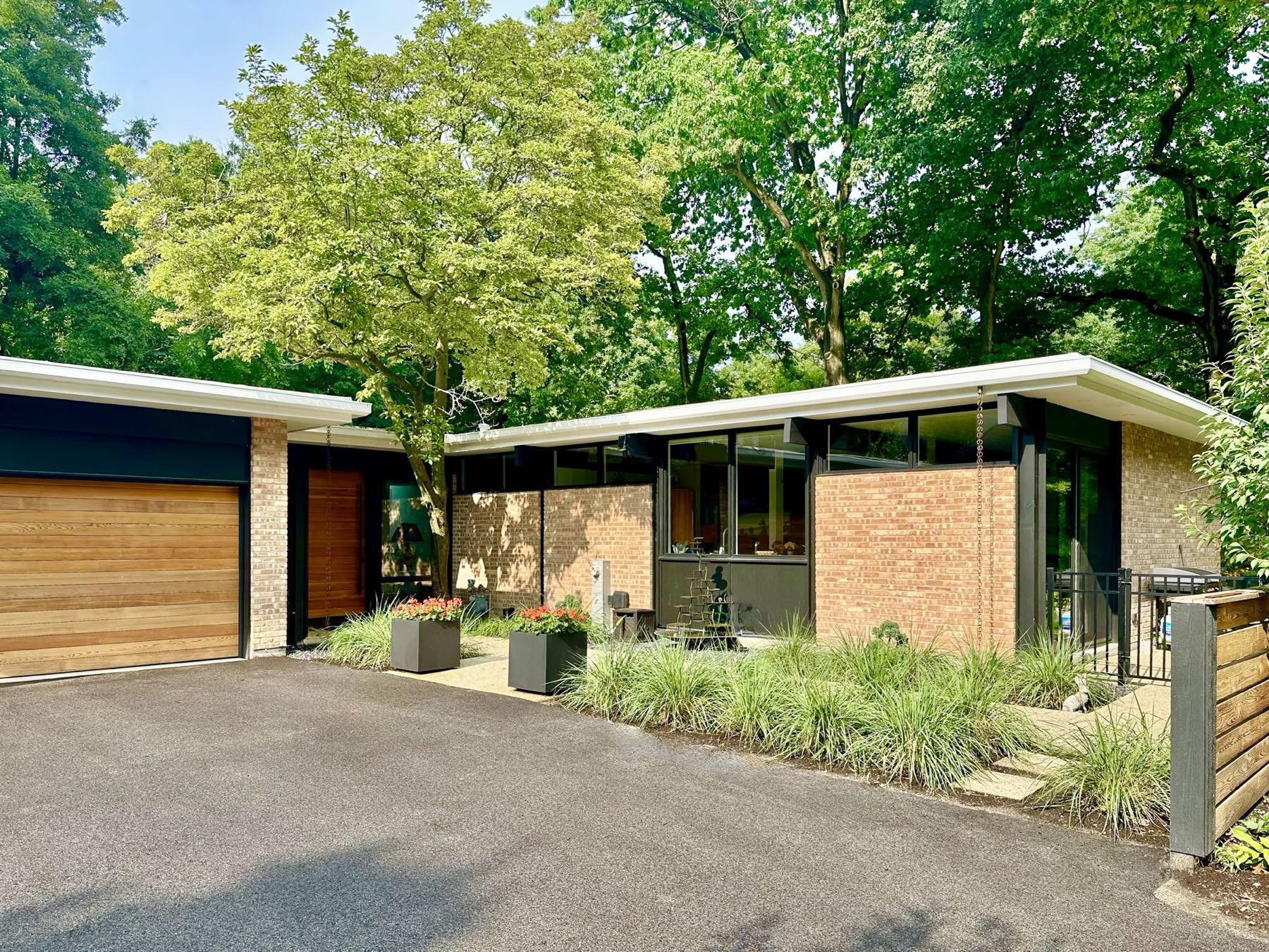 The house seen from the drive, with a cedar garage door at left and the glazed entry court at right.