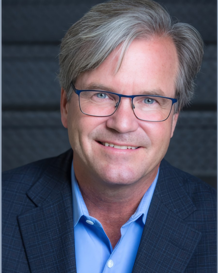 Rob Douglass, in a jacket and open-collared shirt, against a grey stone wall.