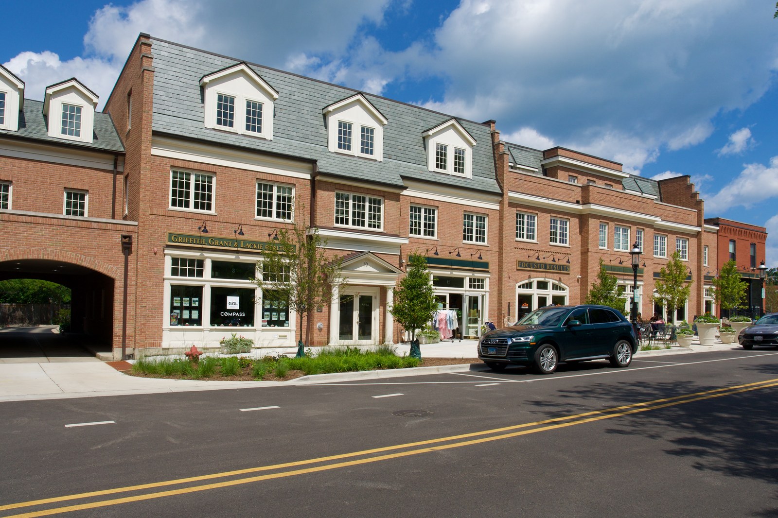 The south elevation along the street, shopfronts at pavement level, two floors of offices above, and a carriage arch cut through to the parking behind.