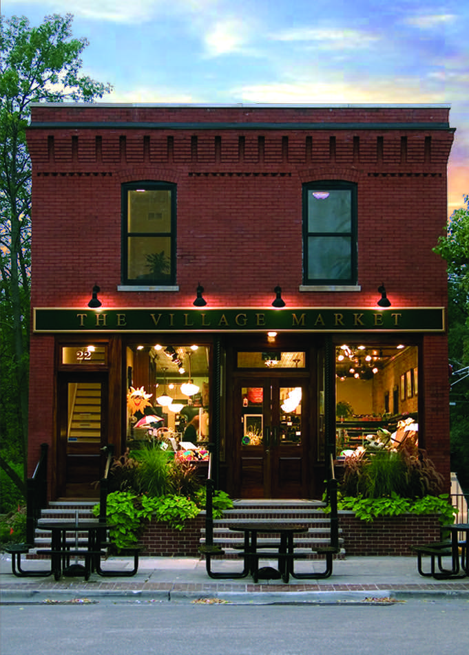 The front elevation at dusk, the shopfront lit behind its windows below two arched second floor windows and a corbelled brick cornice.