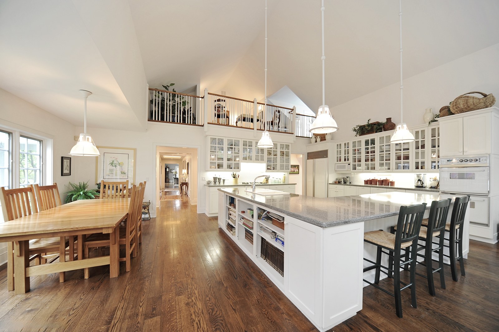 The kitchen from the dining end, with pendant lights over the island and glazed wall cabinets to the ceiling.