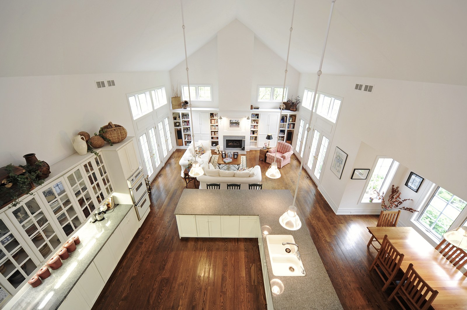 Looking down from the loft into the kitchen and living area, showing the full height of the vaulted ceiling and the built-in bookcases flanking the fireplace.