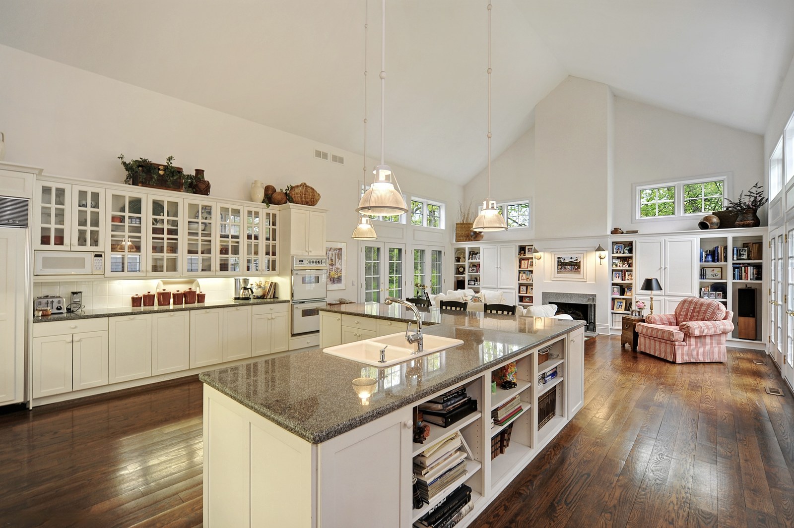 Kitchen with a long granite island and seating, glass-fronted white cabinetry, and the loft railing above overlooking the room.